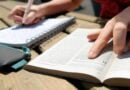 Mão escrevendo em caderno analisando Bíblia
