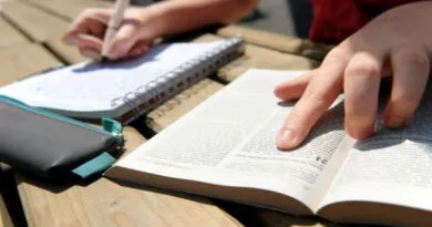 Mão escrevendo em caderno analisando Bíblia