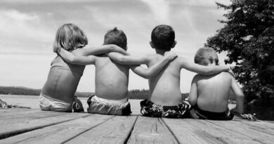 quatro crianças sentadas e com os braços postos nos ombros uns dos outros