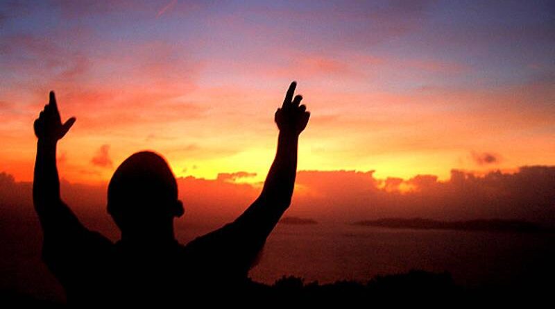 homem com as mão levantadas observando o por do sol.